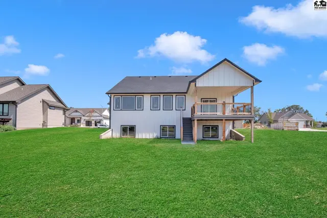 Modern white house with black trim, large windows, and a wooden deck overlooking a green lawn.