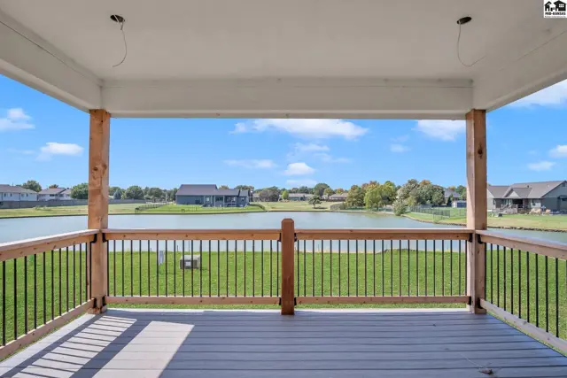 Covered deck with composite flooring and wood railings overlooks a serene lake and suburban homes.