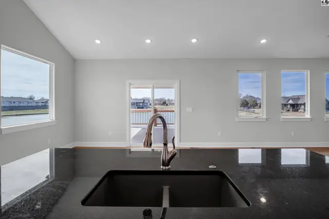 Modern kitchen island with dark granite countertop, stainless steel faucet, and view of a lake through large windows.