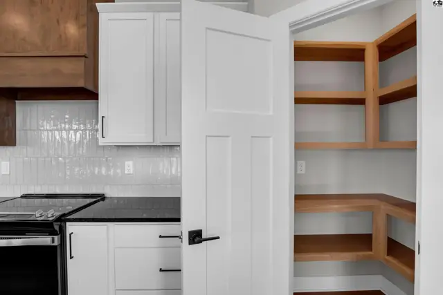 Modern kitchen with white cabinets, subway tile backsplash, and a spacious walk-in pantry with wood shelving.
