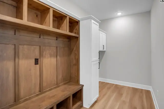 Built-in wooden cubbies and bench complement white cabinetry in this spacious mudroom.