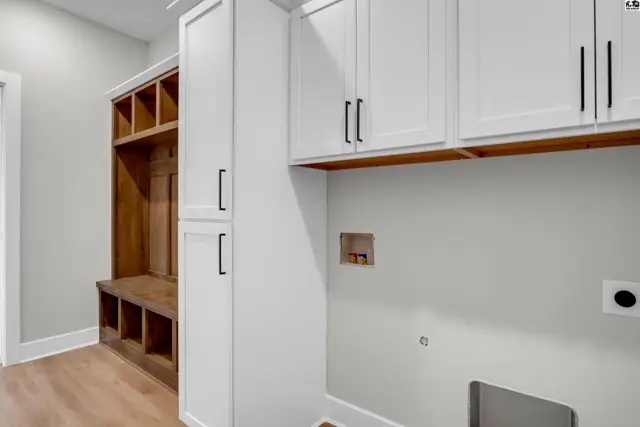 Modern laundry room with white cabinetry, wood bench, and built-in cubbies.