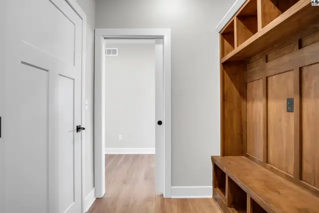 Entryway with white doors, light wood floors, and a custom built-in wooden bench and shelving unit.