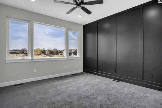 Spacious bedroom with large windows, gray carpet, and a dramatic dark wood paneled accent wall.