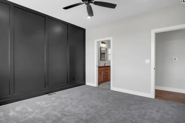 Spacious bedroom with a large, dark paneled wall, gray carpet, and an open doorway to a bathroom.
