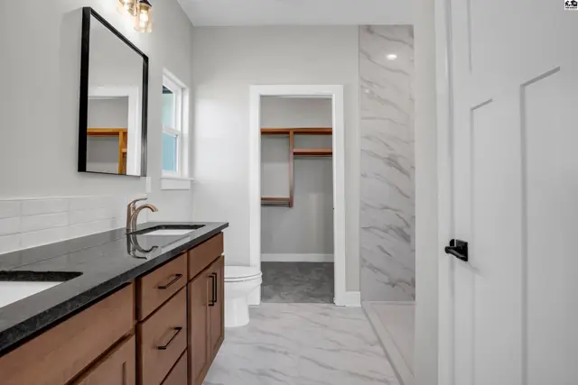 Modern bathroom with double vanity, granite counters, wood cabinets, and marble shower.