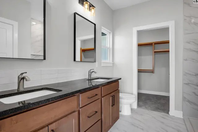 Modern bathroom with double vanity, granite countertops, dark wood cabinets, and a walk-in closet.