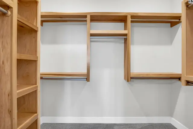 Spacious walk-in closet with light wood shelving and hanging rods against a white wall.