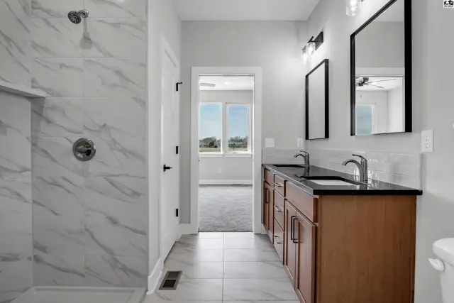 Modern bathroom with marble shower, dual vanity with dark countertops, and wood cabinets.