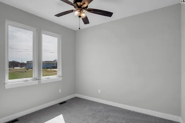 Bright, empty bedroom with gray carpet, white trim, and large windows.