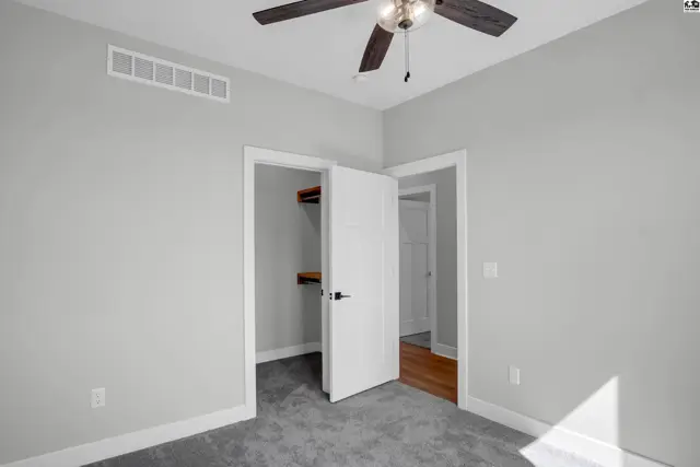 Bright bedroom with gray carpet, white trim, and a walk-in closet with wood shelving.