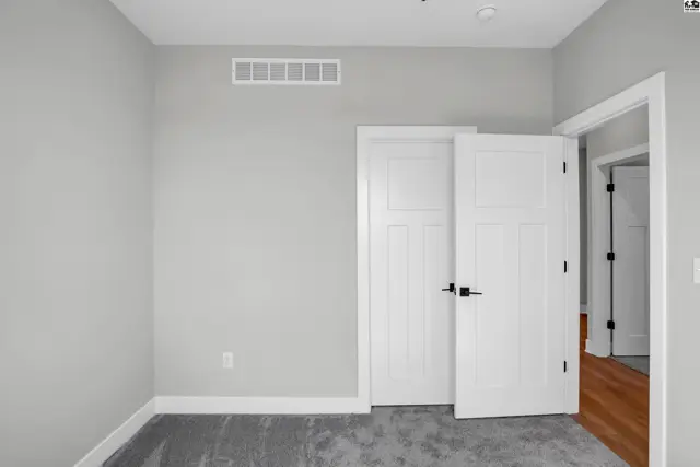 Modern bedroom with light gray walls, plush carpet, and white paneled doors with black hardware.