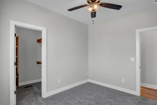 Empty bedroom with gray carpet, white trim, and a ceiling fan.