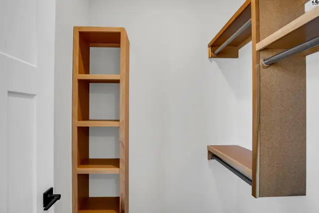 Empty walk-in closet with light wood shelving and hanging rods against a white wall.