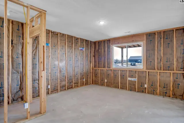 Unfinished room with exposed wood framing, insulation, concrete floor, and a window overlooking an exterior.