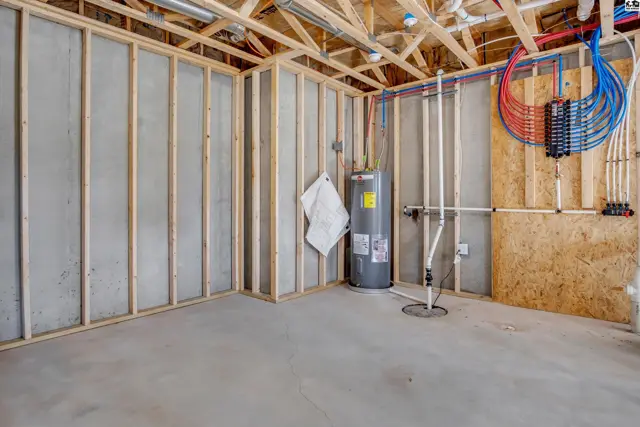 Unfinished basement room with concrete floor, framed walls, water heater, and plumbing.