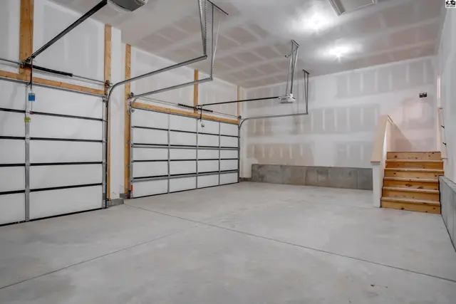 Spacious garage with two white paneled doors, concrete floor, and unfinished walls with wooden stairs.