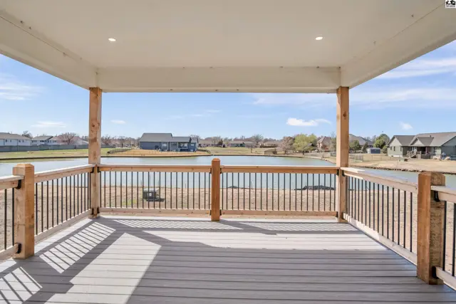 Covered deck with wood posts and railings overlooks a tranquil lake and surrounding homes.