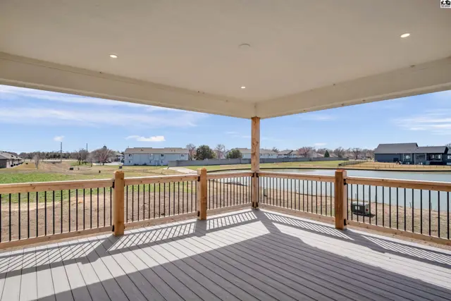 Spacious covered deck with gray composite flooring and wood-trimmed railings overlooks a serene pond.
