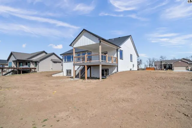 Modern white house with a covered deck and large windows overlooks a freshly graded yard.