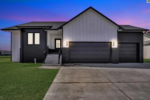 Modern home exterior with black and white siding, a dark garage door, and concrete driveway.