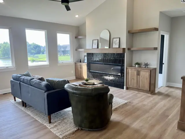 Spacious living room with vaulted ceiling, modern fireplace, and large windows overlooking a lake.