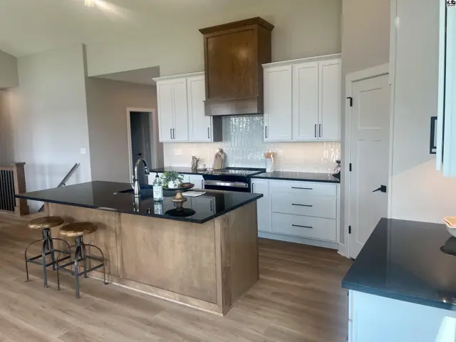 Spacious kitchen with white cabinets, dark countertops, and a large island with wood accents.