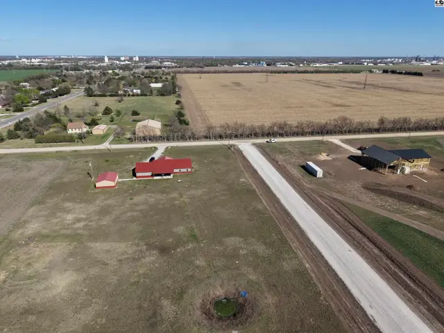 Aerial view of rural properties with red-roofed buildings and open fields under a clear blue sky.
