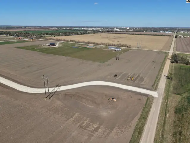 Expansive undeveloped land with a winding gravel road, power lines, and distant town buildings.