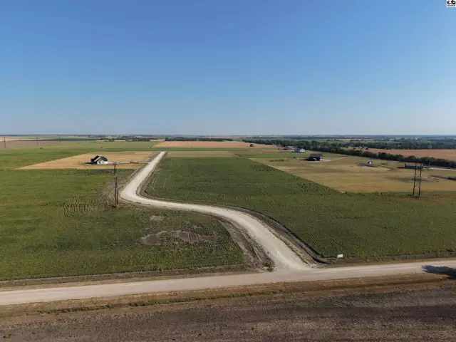 Expansive rural acreage features a winding gravel driveway leading to a small structure.