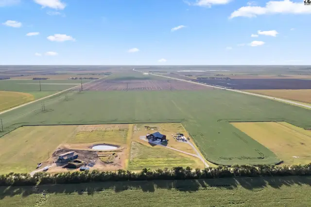 Spacious rural property with two homes, a pond, and expansive agricultural fields under a blue sky.