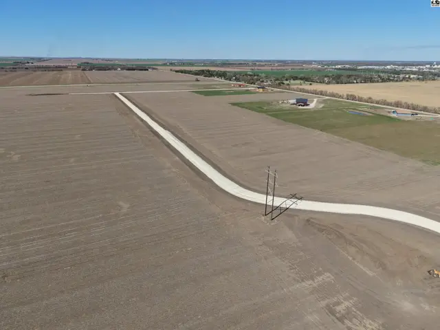 Expansive rural acreage with a gravel driveway leading past power lines toward distant buildings.