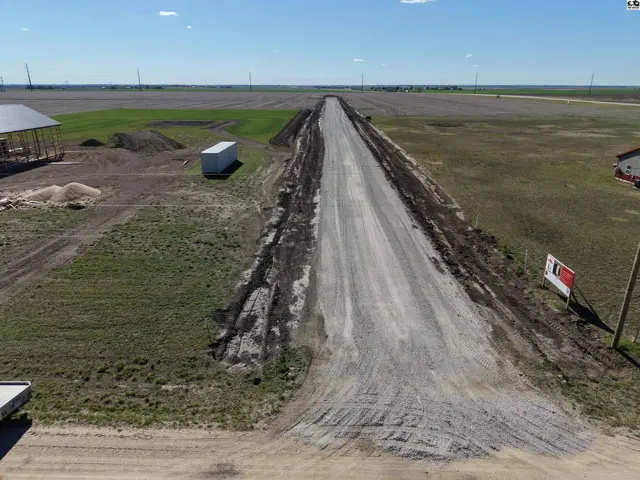 Gravel road leads to open fields with a small building and a white storage container.