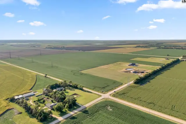 Aerial view of a rural property with a house, outbuildings, and expansive green agricultural fields.