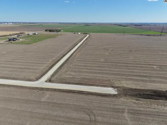 Expansive agricultural land with freshly tilled fields and a gravel road leading to distant farm buildings.