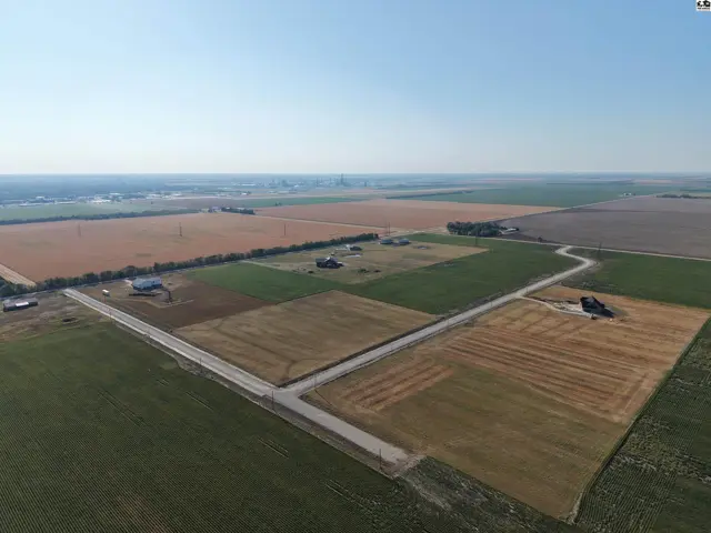 Expansive agricultural land with scattered residences and roadways under a clear sky.