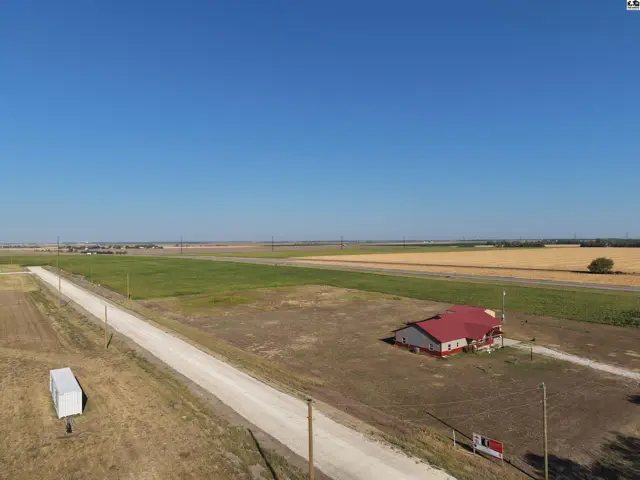 This property features a single-story home with a red roof and surrounding open land.