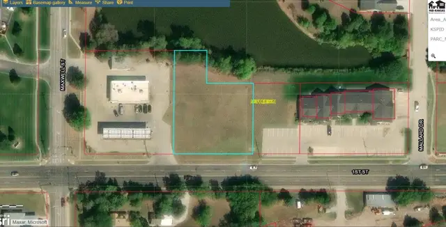 Level lot with mature trees borders a pond and adjacent commercial buildings.