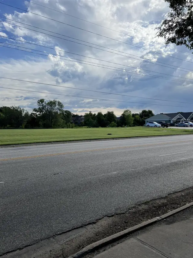 Expansive green lawn borders a paved road with distant houses and trees.