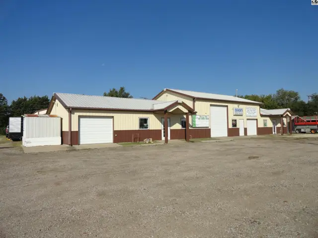 Commercial building with tan siding, brown trim, and multiple garage doors under a metal roof.