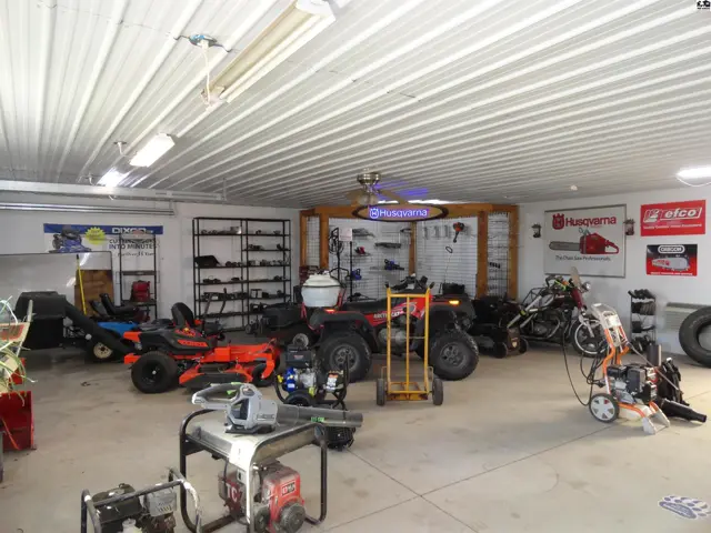 Spacious garage interior with lawnmowers, ATVs, generators, and shelving displaying tools.