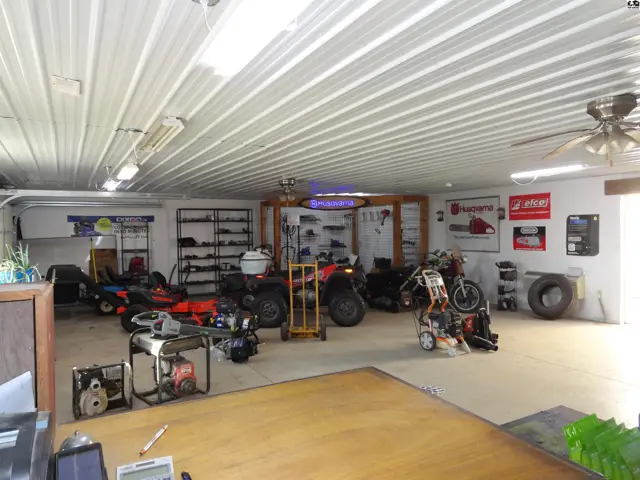 Spacious interior with corrugated metal ceiling, showcasing various outdoor power equipment and shelving.