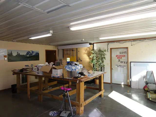 Spacious workshop with large wooden workbench, concrete floors, and fluorescent lighting.