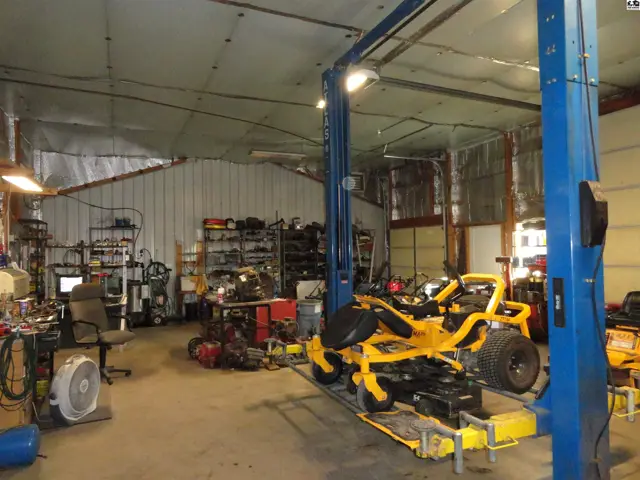 Spacious workshop with a blue car lift, yellow riding mower, and organized shelving.