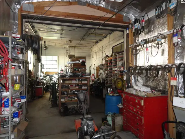 Spacious garage workshop with ample shelving, tools, and a large roll-up door.