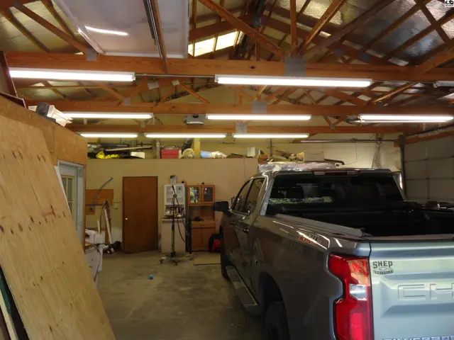 Spacious garage interior with exposed wooden beams, fluorescent lighting, and a pickup truck.