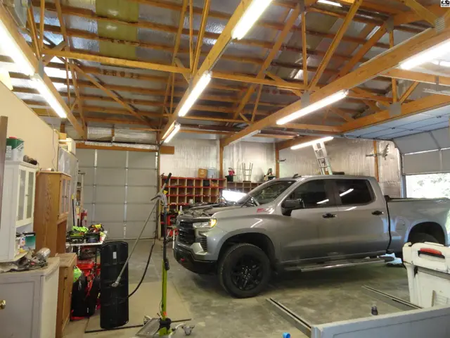 Spacious garage with a pickup truck, exposed wooden beams, and multiple garage doors.
