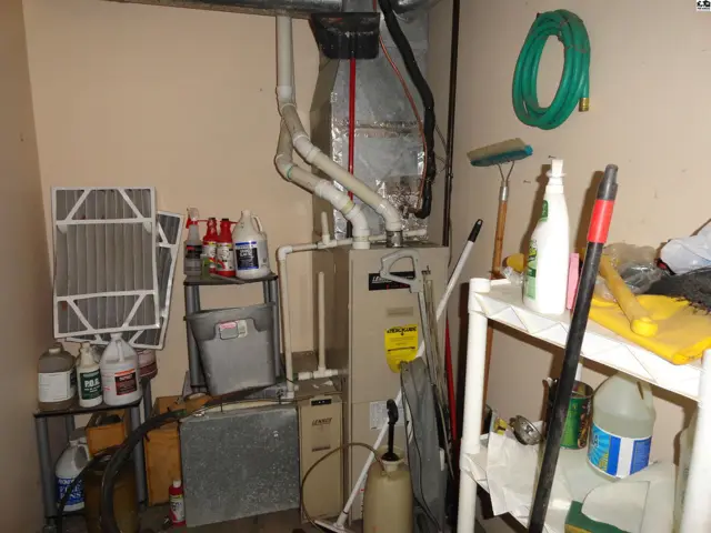Furnace, air filter, cleaning supplies, and tools are organized in a utility room with beige walls.