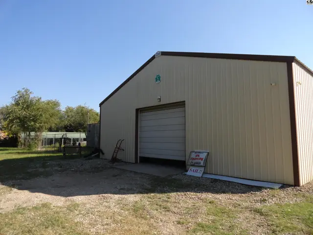 Tan metal building with a large roll-up door and brown trim, set on a gravel lot.