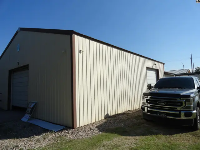 Tan metal building with two garage doors and a dark pickup truck parked outside.
